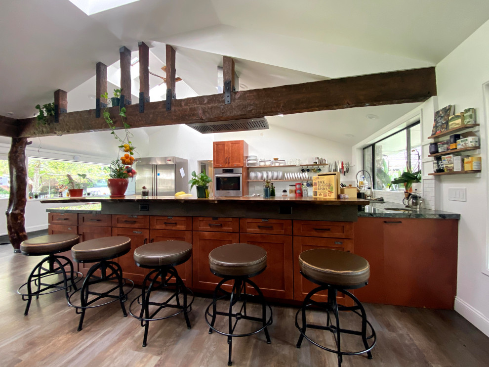 Inspiration for a mid-sized beach style u-shaped eat-in kitchen in San Francisco with a drop-in sink, shaker cabinets, granite benchtops, white splashback, ceramic splashback, stainless steel appliances, vinyl floors, a peninsula, brown floor, green benchtop, vaulted and medium wood cabinets.