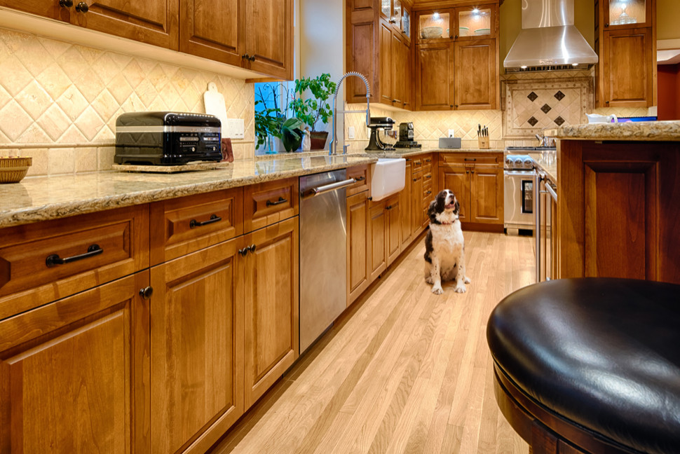 Photo of a large traditional l-shaped eat-in kitchen in Minneapolis with an undermount sink, raised-panel cabinets, medium wood cabinets, granite benchtops, beige splashback, stone tile splashback, stainless steel appliances, light hardwood floors, with island, brown floor and yellow benchtop.