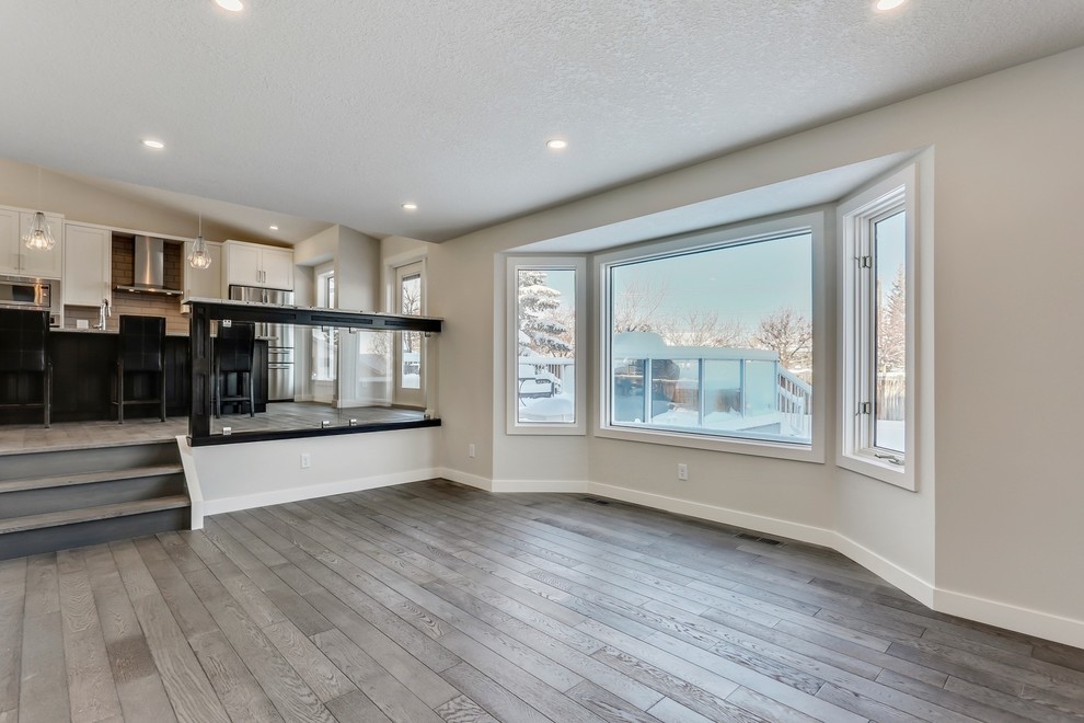 This is an example of a large transitional open concept living room in Calgary with white walls, medium hardwood floors, a standard fireplace, a tile fireplace surround, a wall-mounted tv and brown floor.