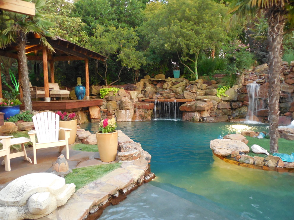This is an example of an expansive tropical backyard custom-shaped natural pool in Dallas with a water feature and stamped concrete.