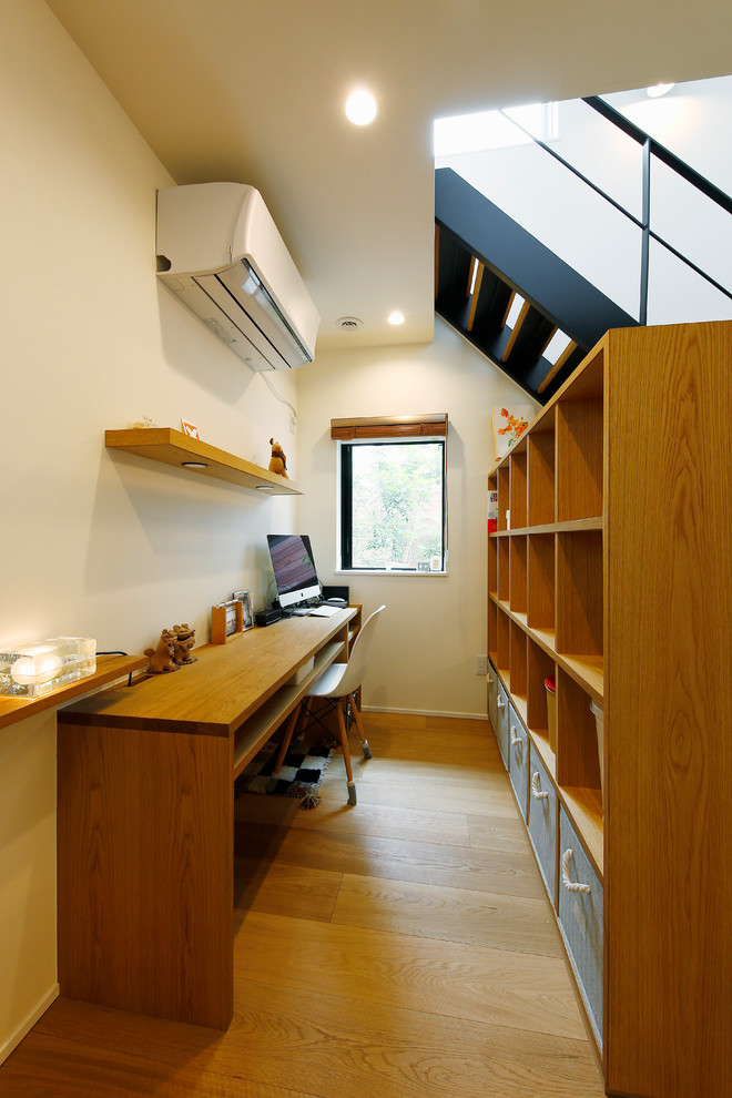 Mid-sized scandinavian home office in Tokyo with a library, white walls, medium hardwood floors, a built-in desk and brown floor.