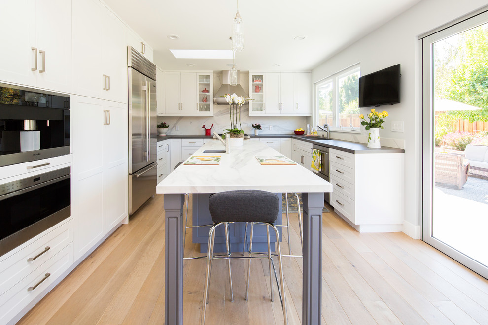 Design ideas for a mid-sized transitional u-shaped kitchen in San Francisco with shaker cabinets, white cabinets, white splashback, light hardwood floors, with island, a single-bowl sink, marble benchtops, marble splashback, stainless steel appliances and beige floor.