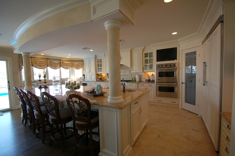 Large traditional u-shaped eat-in kitchen in New York with an undermount sink, recessed-panel cabinets, white cabinets, granite benchtops, beige splashback, panelled appliances, limestone floors and with island.