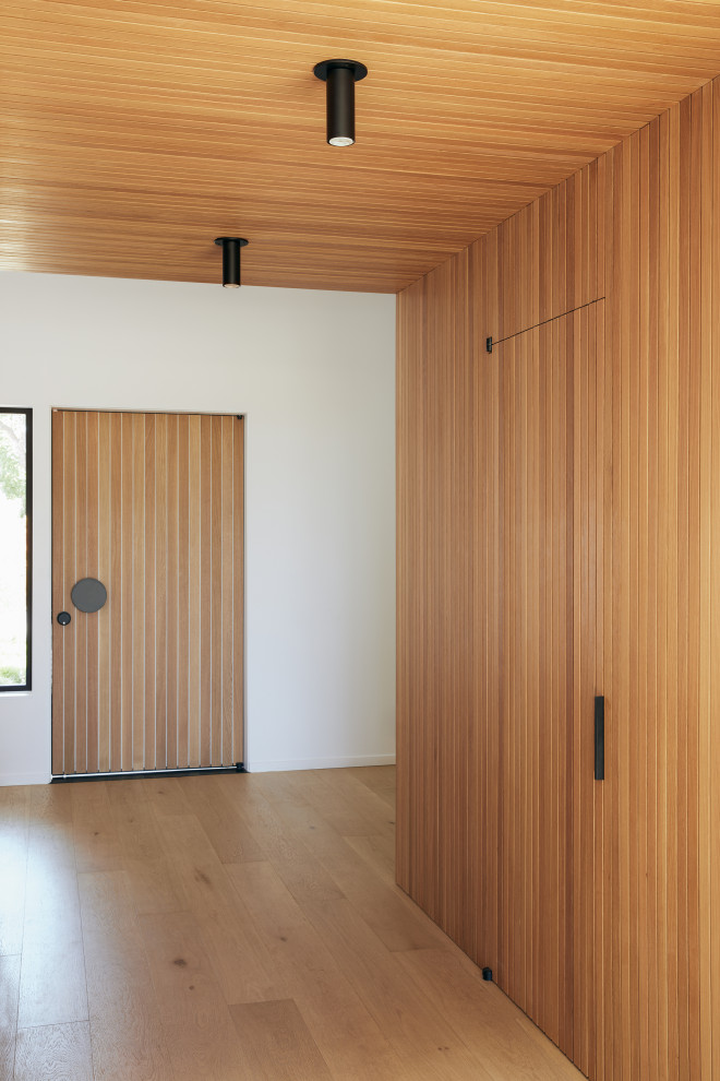 На фото: фойе среднего размера в стиле модернизм с белыми стенами, светлым паркетным полом, поворотной входной дверью, входной дверью из светлого дерева, коричневым полом, сводчатым потолком и деревянными стенами с