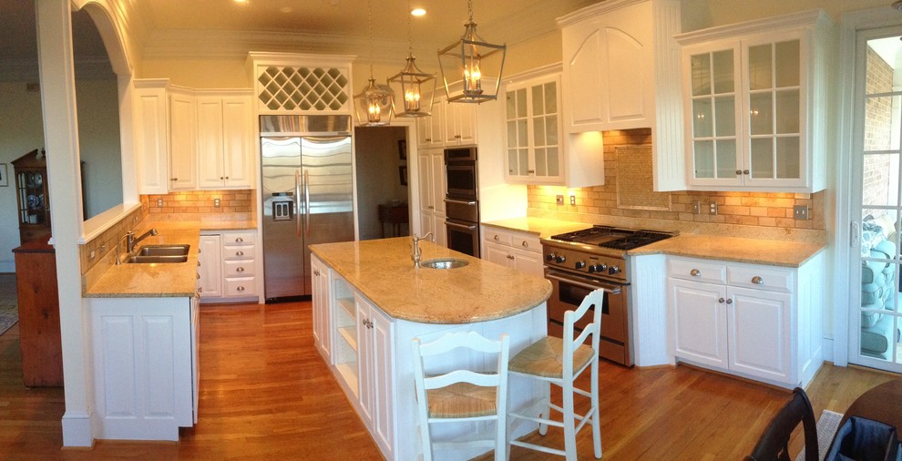 Inspiration for a mid-sized transitional l-shaped medium tone wood floor enclosed kitchen remodel with an undermount sink, raised-panel cabinets, white cabinets, granite countertops, beige backsplash, stone tile backsplash, stainless steel appliances and an island