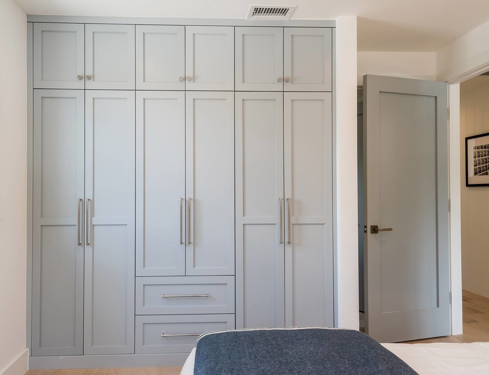 Photo of a small beach style gender-neutral built-in wardrobe in Los Angeles with shaker cabinets, blue cabinets, medium hardwood floors and brown floor.