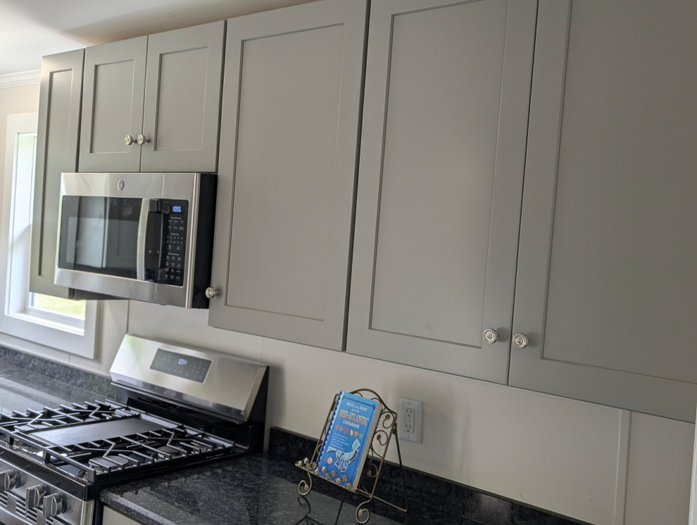 Small transitional l-shaped gray floor enclosed kitchen photo with a single-bowl sink, flat-panel cabinets, gray cabinets, granite countertops, stainless steel appliances and black countertops