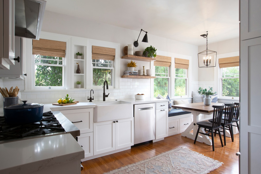Transitional u-shaped eat-in kitchen in Denver with a farmhouse sink, shaker cabinets, white cabinets, white splashback, subway tile splashback, stainless steel appliances, medium hardwood floors, no island, brown floor and white benchtop.