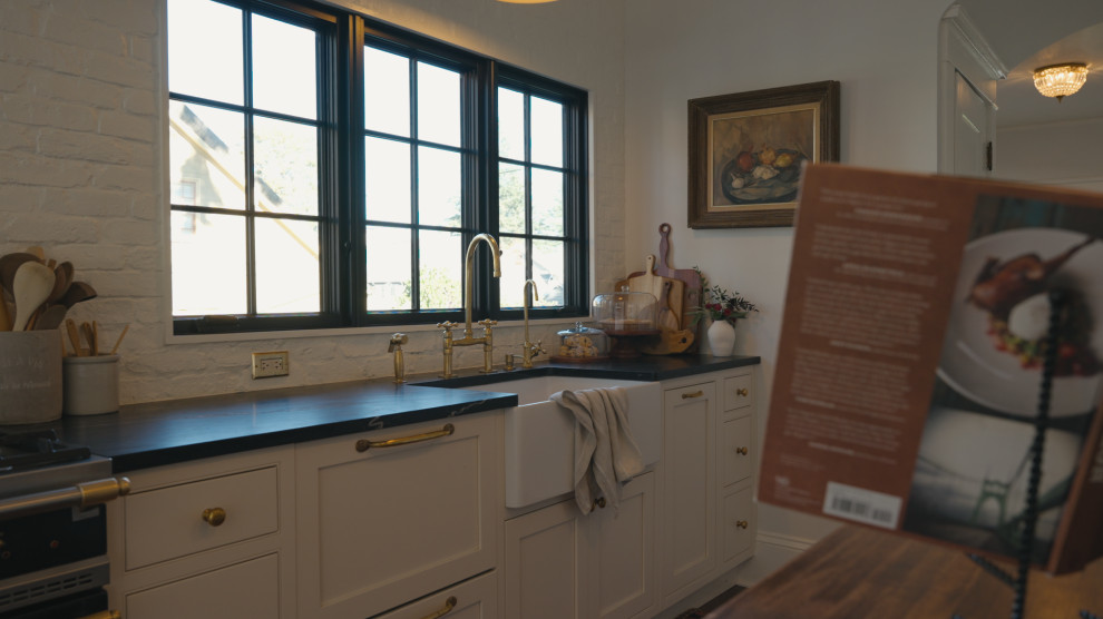 Example of a mid-sized transitional galley dark wood floor and brown floor enclosed kitchen design in Portland with a farmhouse sink, beaded inset cabinets, beige cabinets, soapstone countertops, white backsplash, brick backsplash, paneled appliances, an island and black countertops