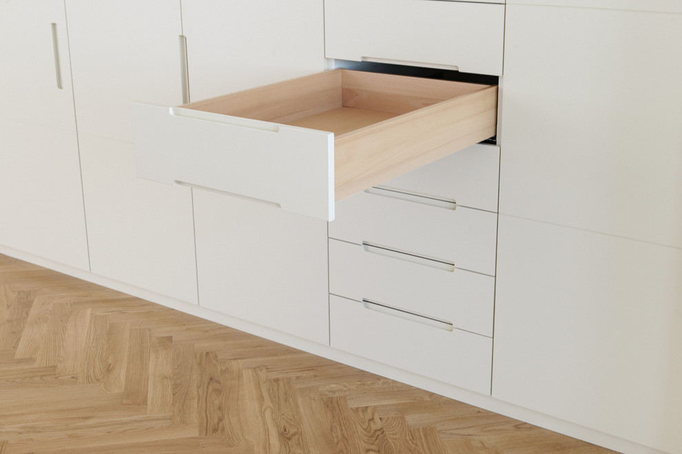 Expansive contemporary gender-neutral dressing room in Munich with flat-panel cabinets, beige cabinets, light hardwood floors and beige floor.