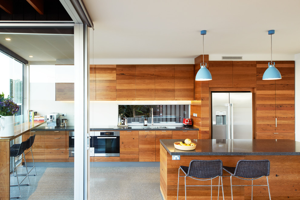 Design ideas for a mid-sized contemporary l-shaped eat-in kitchen in Sydney with a double-bowl sink, flat-panel cabinets, medium wood cabinets, quartz benchtops, white splashback, glass sheet splashback, stainless steel appliances, concrete floors and with island.