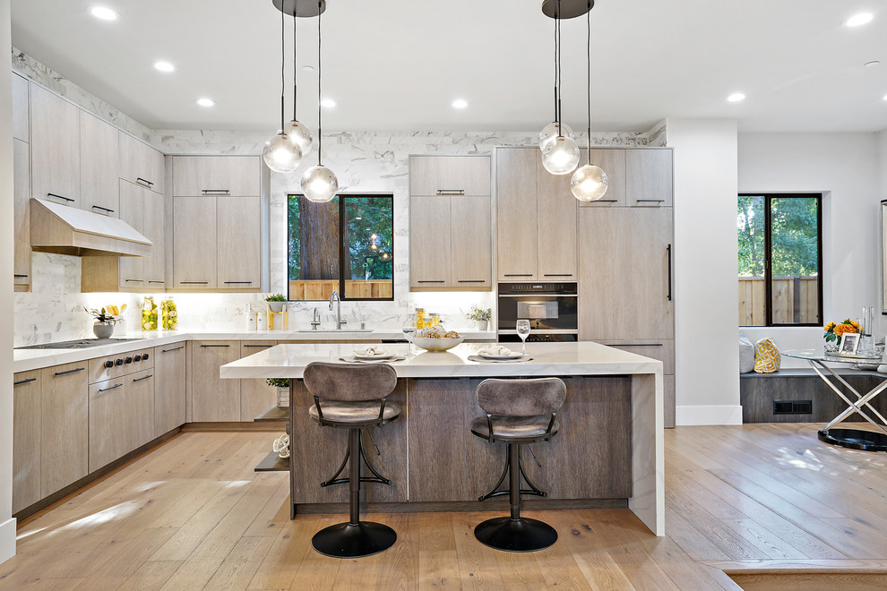Photo of a large modern l-shaped open plan kitchen in San Francisco with an undermount sink, flat-panel cabinets, light wood cabinets, marble benchtops, white splashback, marble splashback, panelled appliances, light hardwood floors, with island, beige floor and white benchtop.