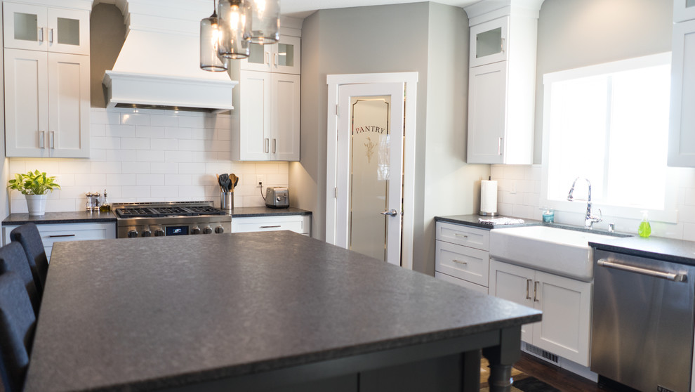 Photo of a large transitional u-shaped eat-in kitchen in Other with a farmhouse sink, flat-panel cabinets, white cabinets, granite benchtops, white splashback, ceramic splashback, stainless steel appliances and with island.