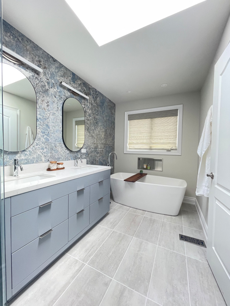 Bild på ett funkis badrum, med blå skåp, ett fristående badkar, blå kakel, klinkergolv i keramik, bänkskiva i kvarts, grått golv och dusch med gångjärnsdörr