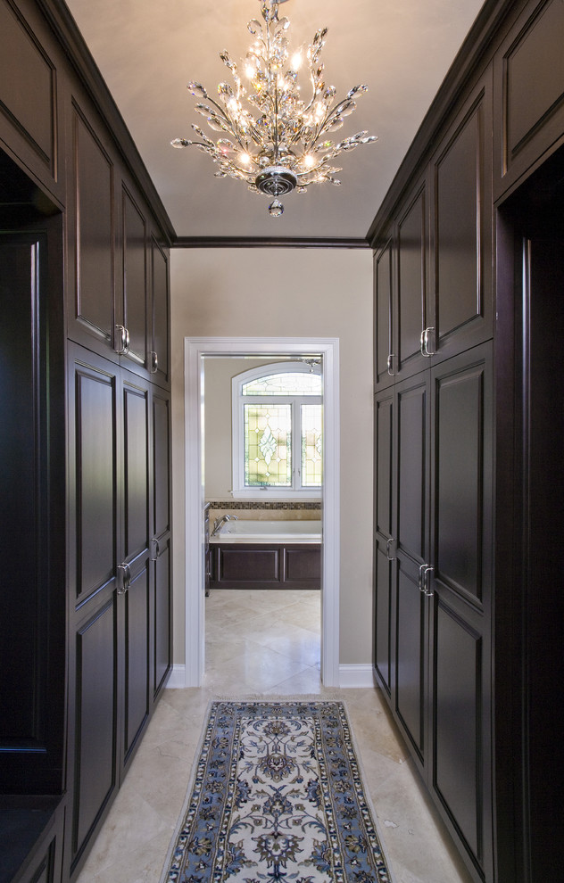 This is an example of a large traditional gender-neutral dressing room in Chicago with raised-panel cabinets, dark wood cabinets, limestone floors and beige floor.