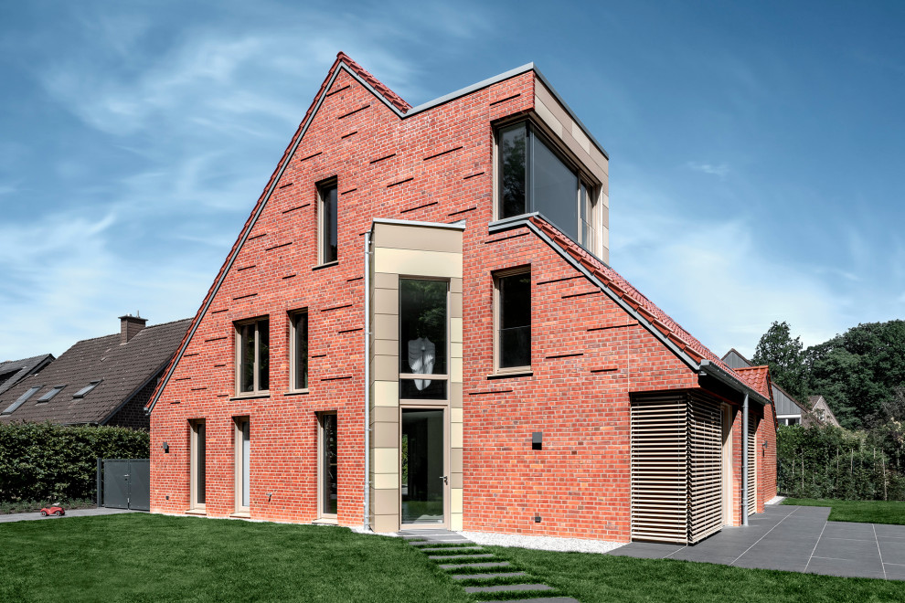 This is an example of a large contemporary three-storey brick red house exterior in Other with a tile roof, a red roof and a gable roof.