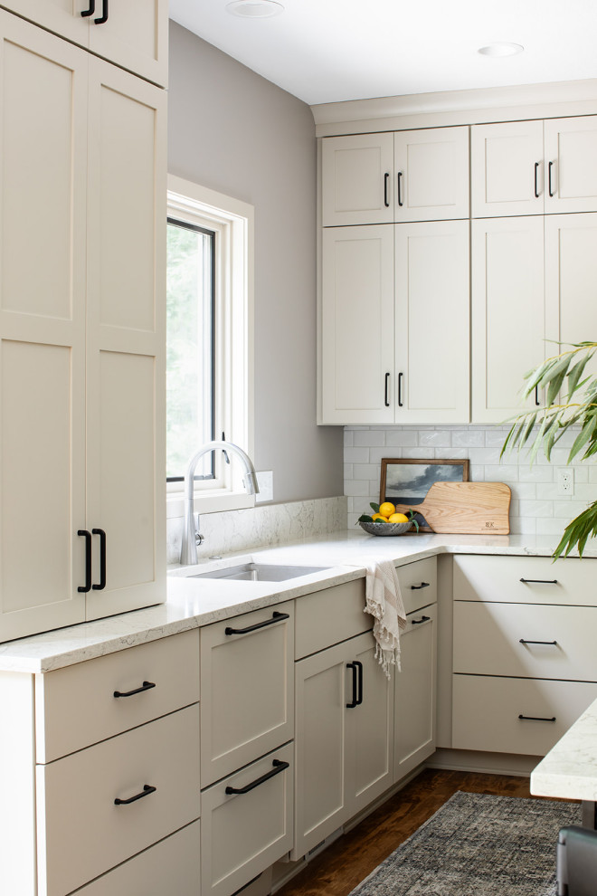 Example of a mid-sized transitional u-shaped medium tone wood floor and brown floor eat-in kitchen design with an undermount sink, shaker cabinets, white cabinets, quartz countertops, white backsplash, subway tile backsplash, black appliances, an island and white countertops