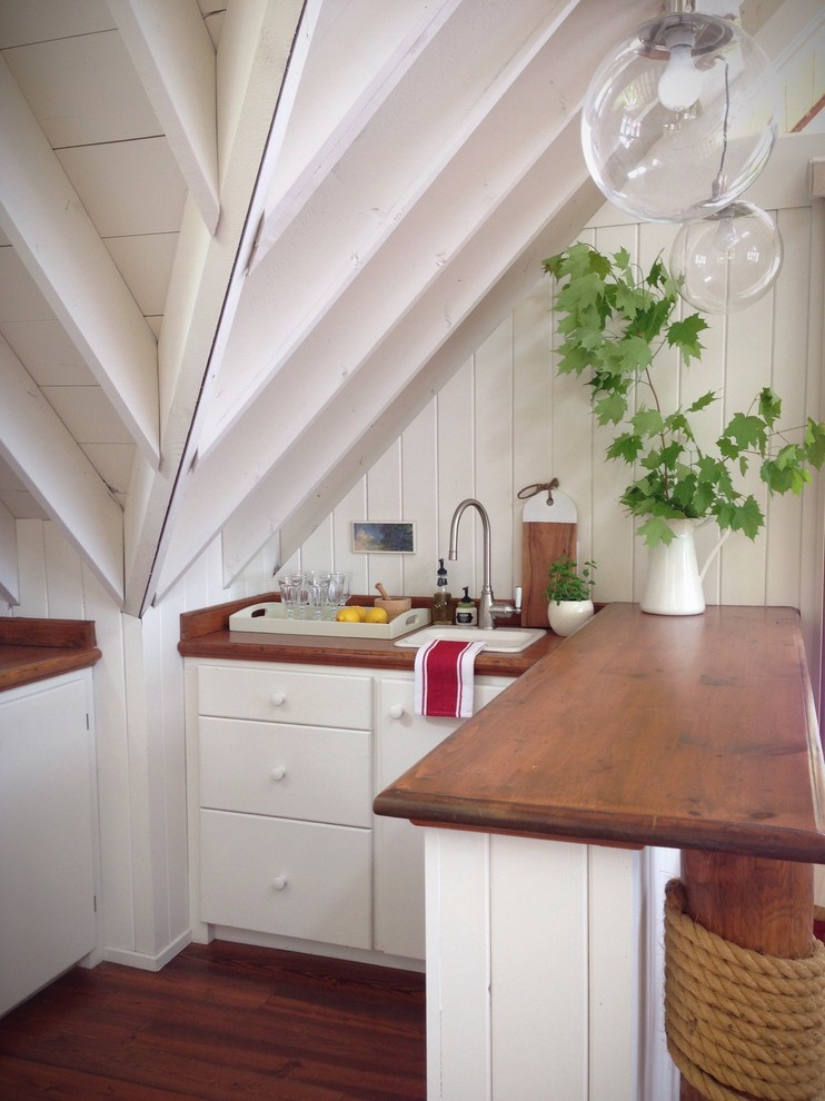 This is an example of a small beach style u-shaped kitchen in Other with a drop-in sink, flat-panel cabinets, white cabinets, wood benchtops, dark hardwood floors and a peninsula.