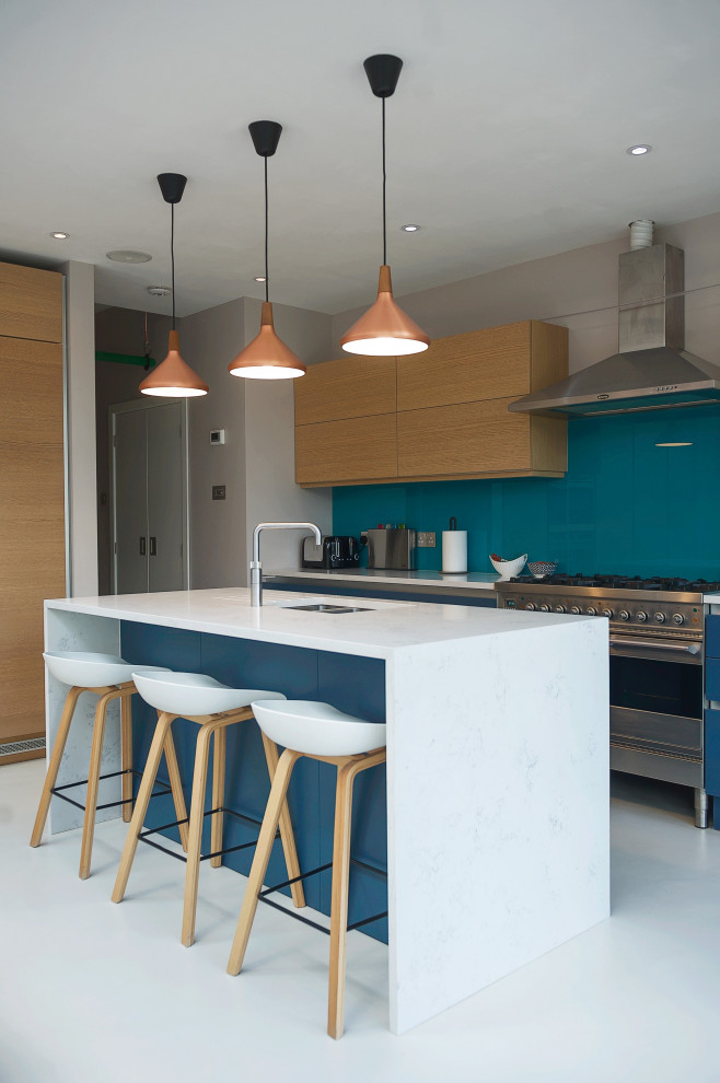 Photo of a contemporary kitchen in London with an undermount sink, flat-panel cabinets, light wood cabinets, blue splashback, stainless steel appliances, with island, white floor and white benchtop.