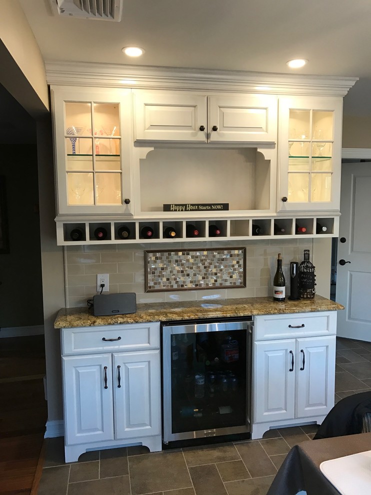 Photo of a small transitional single-wall wet bar in New York with no sink, raised-panel cabinets, white cabinets, granite benchtops, beige splashback, mosaic tile splashback, slate floors, beige floor and beige benchtop.