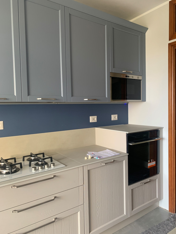 Design ideas for a mid-sized contemporary galley separate kitchen in Milan with a drop-in sink, recessed-panel cabinets, blue cabinets, granite benchtops, beige splashback, granite splashback, white appliances, concrete floors, grey floor and beige benchtop.