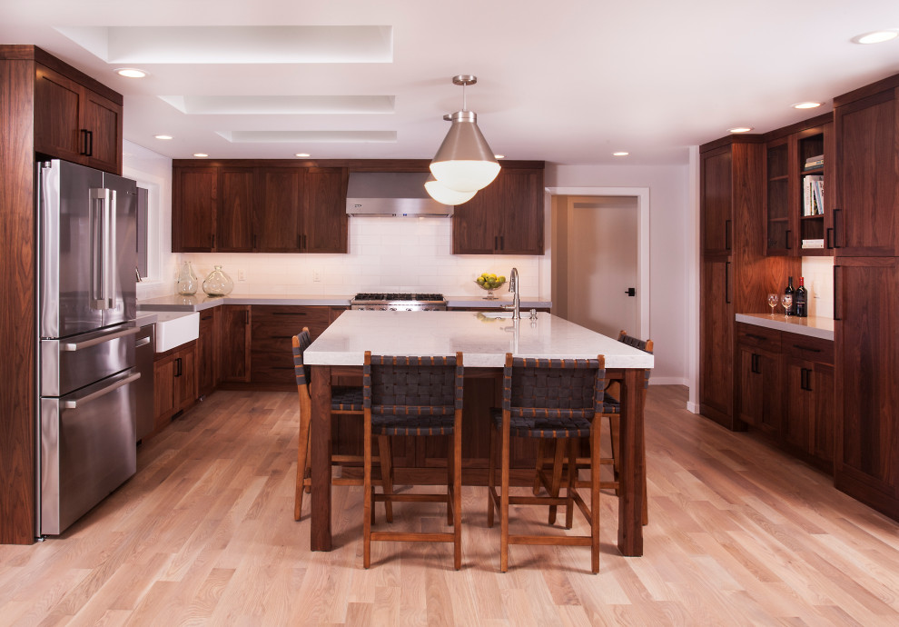 Example of a large transitional u-shaped light wood floor and brown floor eat-in kitchen design in Seattle with a farmhouse sink, dark wood cabinets, white backsplash, subway tile backsplash, stainless steel appliances, an island and white countertops