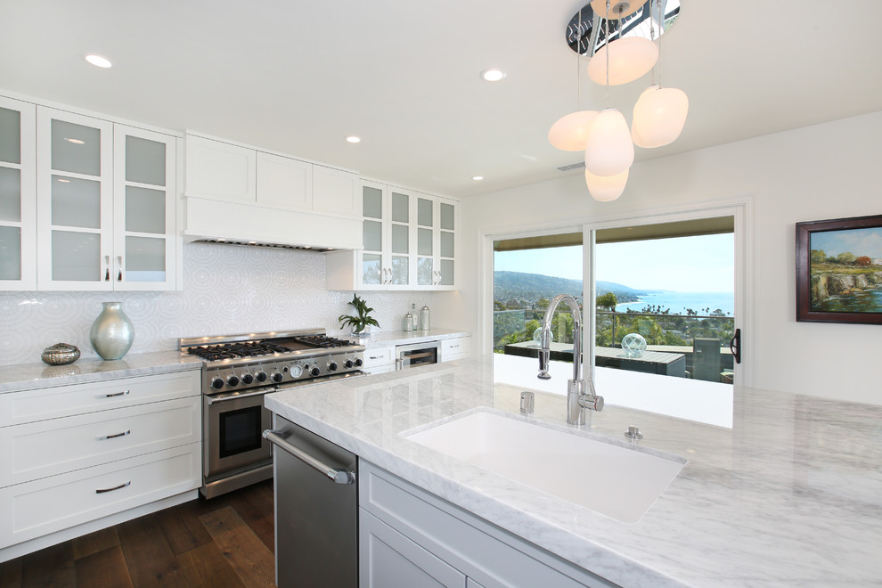 L-shaped medium tone wood floor kitchen photo in Orange County with an undermount sink, recessed-panel cabinets, white cabinets, marble countertops, white backsplash, mosaic tile backsplash and stainless steel appliances