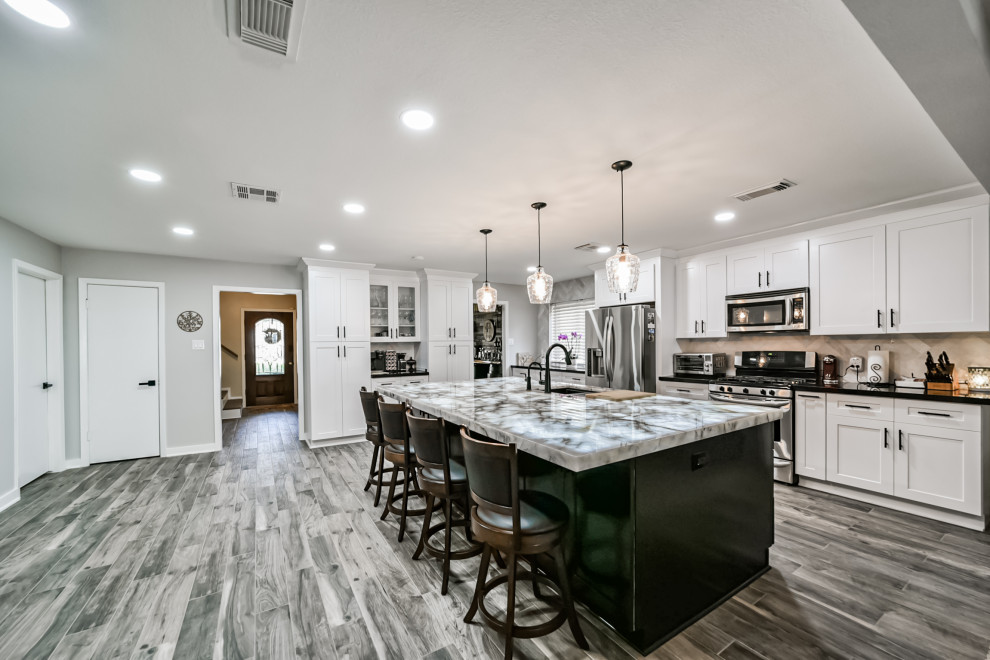 Photo of a large modern u-shaped kitchen pantry in Houston with a belfast sink, shaker cabinets, white cabinets, engineered stone countertops, grey splashback, ceramic splashback, stainless steel appliances, cement flooring, an island, grey floors, black worktops and a coffered ceiling.