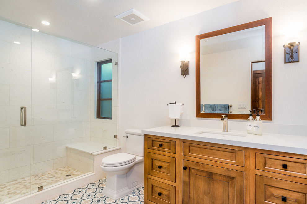 Photo of a mediterranean 3/4 bathroom in Los Angeles with raised-panel cabinets, medium wood cabinets, an alcove shower, a wall-mount toilet, white tile, limestone, white walls, cement tiles, an undermount sink, engineered quartz benchtops, multi-coloured floor and a hinged shower door.