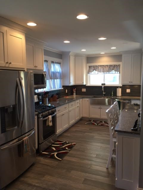 Mid-sized minimalist u-shaped medium tone wood floor and brown floor enclosed kitchen photo in Baltimore with a farmhouse sink, shaker cabinets, white cabinets, granite countertops, gray backsplash, porcelain backsplash, stainless steel appliances and no island