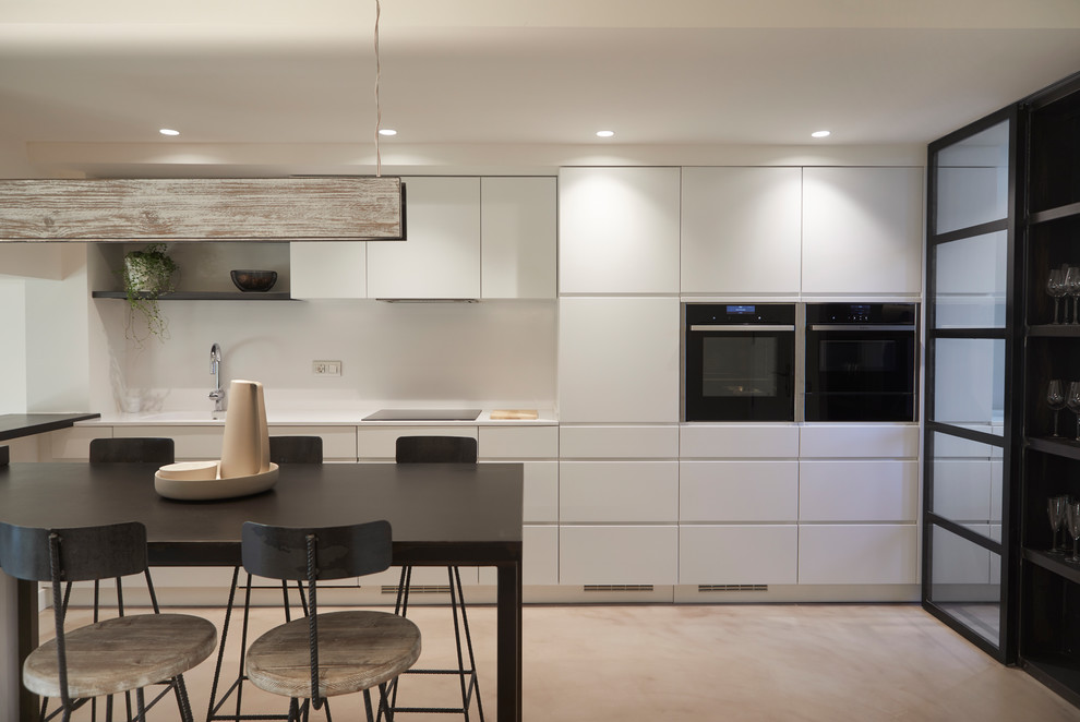 Photo of a contemporary l-shaped eat-in kitchen in Barcelona with flat-panel cabinets, white cabinets, stainless steel appliances, concrete floors, grey floor and white benchtop.