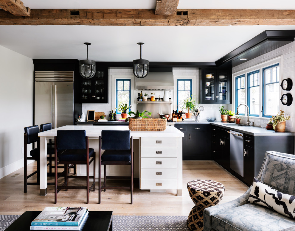 Example of a transitional l-shaped light wood floor and beige floor eat-in kitchen design in New York with an undermount sink, flat-panel cabinets, black cabinets, white backsplash, subway tile backsplash, stainless steel appliances, an island and white countertops