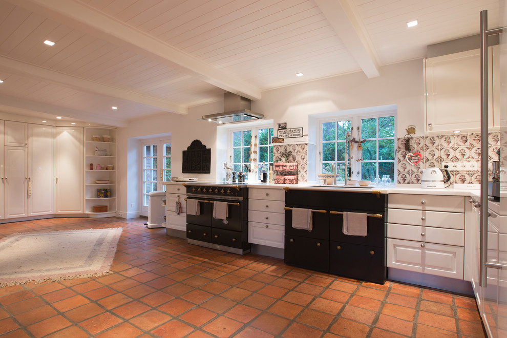 This is an example of an expansive country l-shaped kitchen in Other with an undermount sink, raised-panel cabinets, white cabinets, multi-coloured splashback, ceramic splashback, black appliances, terra-cotta floors and no island.