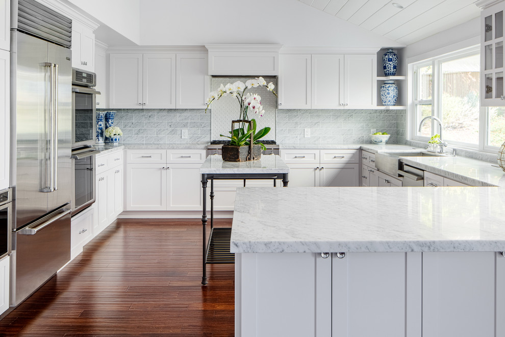 Example of a transitional u-shaped dark wood floor kitchen design in San Diego with a farmhouse sink, shaker cabinets, white cabinets, gray backsplash, subway tile backsplash, stainless steel appliances and a peninsula