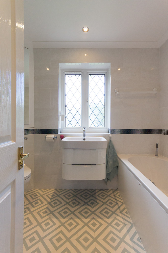 This is an example of a small modern grey and white family bathroom in Surrey with flat-panel cabinets, white cabinets, a built-in bath, a corner shower, grey tiles, porcelain tiles, grey walls, lino flooring, a wall-mounted sink, multi-coloured floors, a sliding door, a single sink, a floating vanity unit and a one-piece toilet.