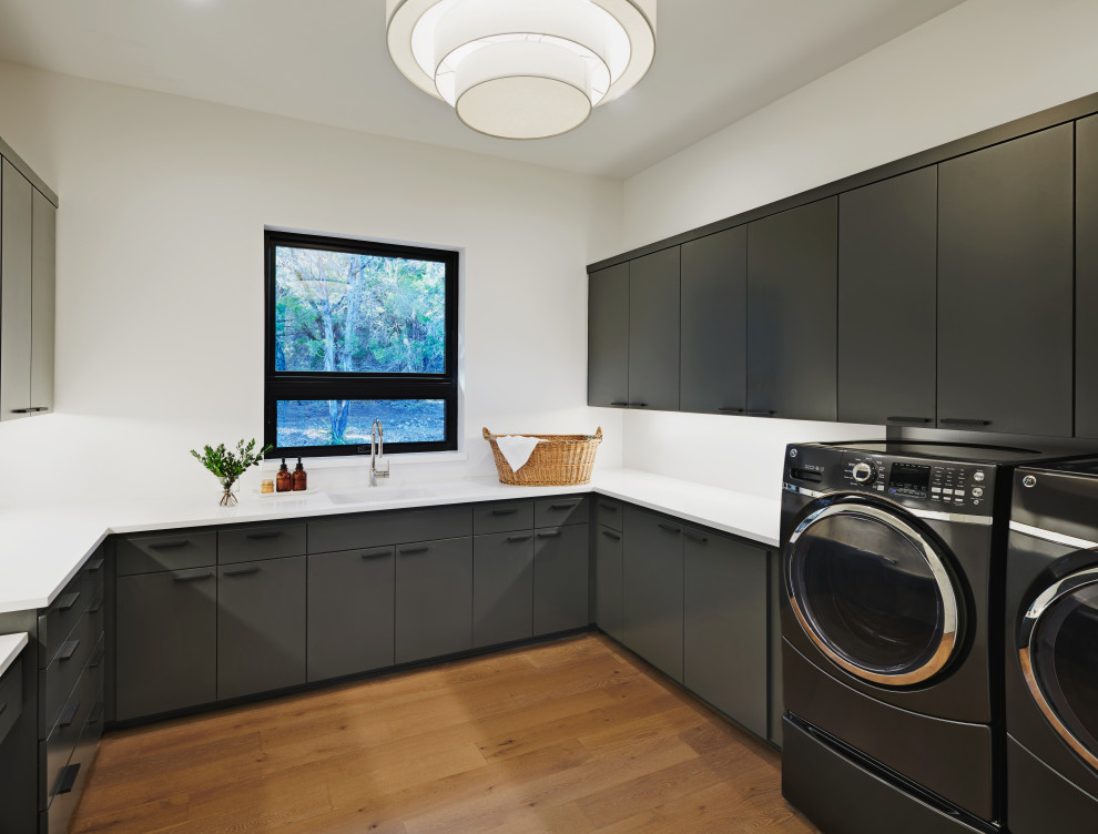 Design ideas for a large contemporary u-shaped utility room in Austin with an undermount sink, flat-panel cabinets, grey cabinets, quartzite benchtops, white walls, medium hardwood floors, a side-by-side washer and dryer, brown floor and white benchtop.