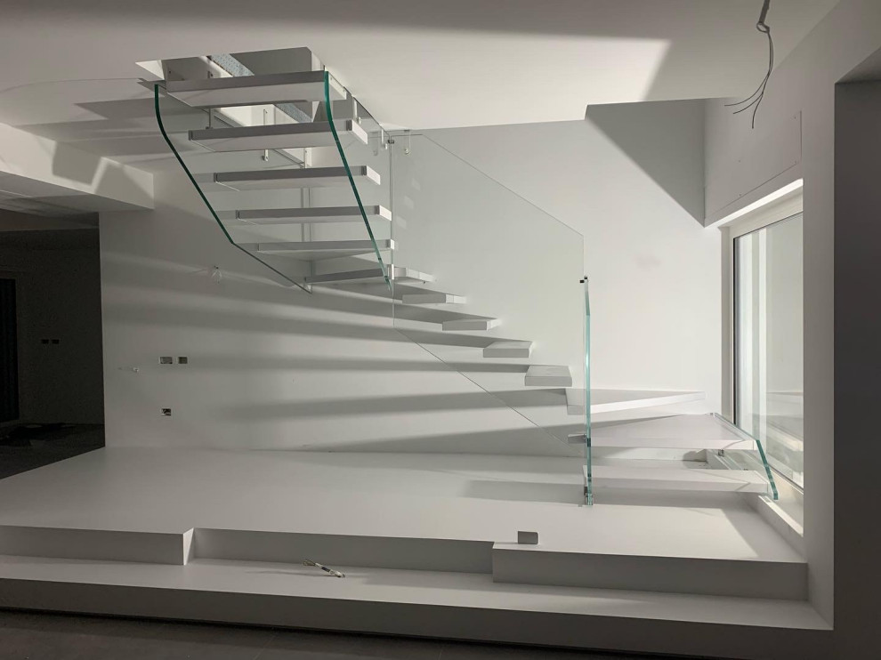 На фото: огромная лестница на больцах в стиле модернизм с крашенными деревянными ступенями и стеклянными перилами без подступенок