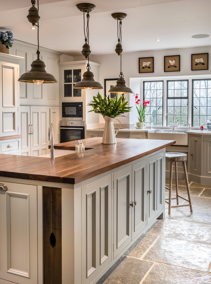 Country kitchen in Other with a farmhouse sink, beaded inset cabinets, grey cabinets, wood benchtops, stainless steel appliances, with island and brown benchtop.