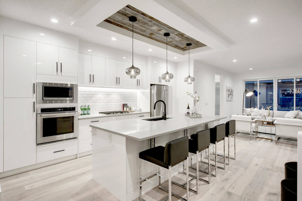 This is an example of a mid-sized contemporary galley eat-in kitchen in Calgary with an undermount sink, flat-panel cabinets, white cabinets, quartz benchtops, white splashback, subway tile splashback, stainless steel appliances, light hardwood floors, with island, beige floor, grey benchtop and recessed.