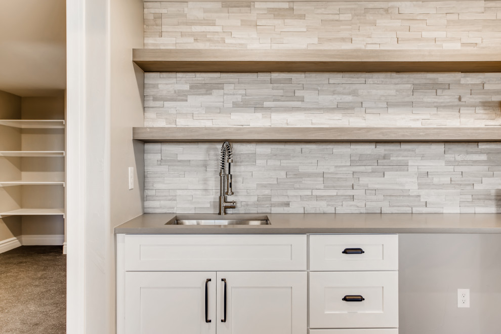 This is an example of a mid-sized contemporary single-wall wet bar in Denver with a drop-in sink, recessed-panel cabinets, white cabinets, quartzite benchtops, white splashback, stone slab splashback, vinyl floors, brown floor and grey benchtop.