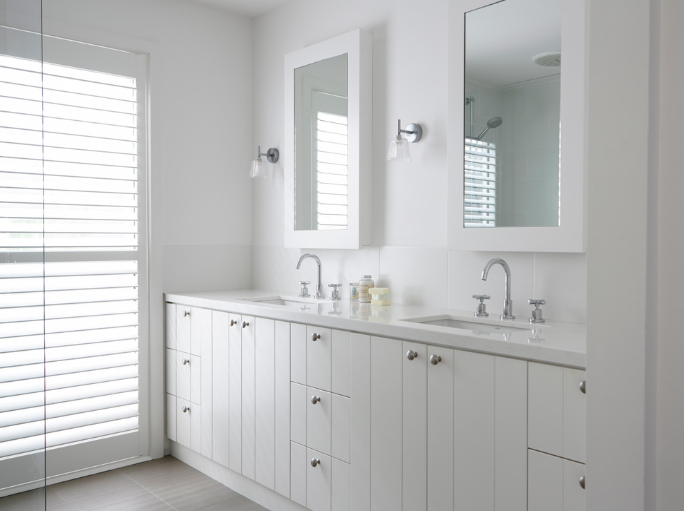 Design ideas for a beach style master bathroom in Melbourne with white cabinets, white walls, porcelain floors, engineered quartz benchtops, flat-panel cabinets, white tile and an undermount sink.