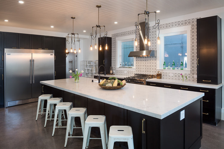 Large industrial single-wall eat-in kitchen in San Francisco with a double-bowl sink, shaker cabinets, black cabinets, solid surface benchtops, beige splashback, stainless steel appliances, concrete floors and with island.