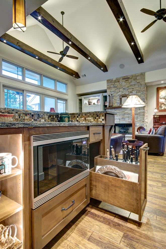 This is an example of a large arts and crafts l-shaped eat-in kitchen in Austin with an undermount sink, shaker cabinets, medium wood cabinets, granite benchtops, brown splashback, mosaic tile splashback, stainless steel appliances, medium hardwood floors and with island.