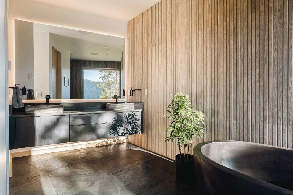 На фото: ванная комната в современном стиле с черными фасадами, отдельно стоящей ванной, полом из керамической плитки, черным полом, открытым душем, тумбой под две раковины, подвесной тумбой и деревянными стенами