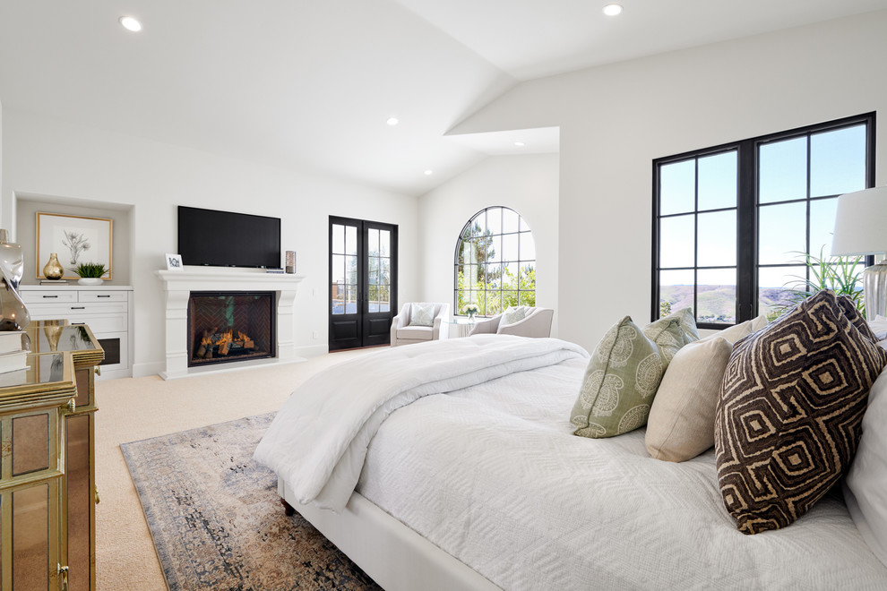Photo of a mid-sized mediterranean master bedroom in Orange County with white walls, carpet, a standard fireplace, a concrete fireplace surround and beige floor.