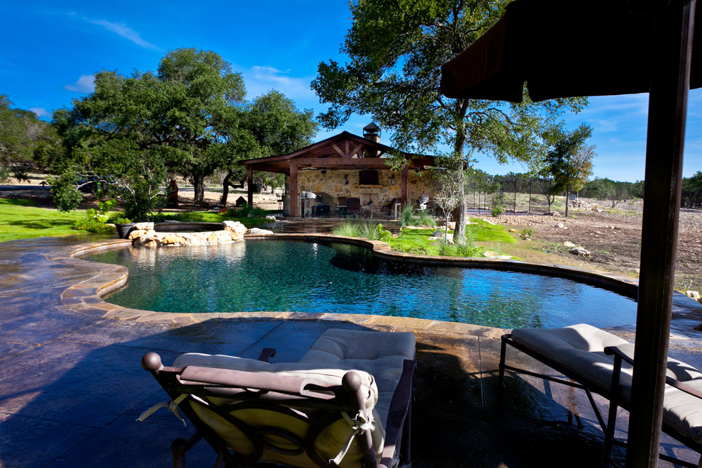 This is an example of a large country backyard custom-shaped natural pool in Austin with a water feature and concrete slab.