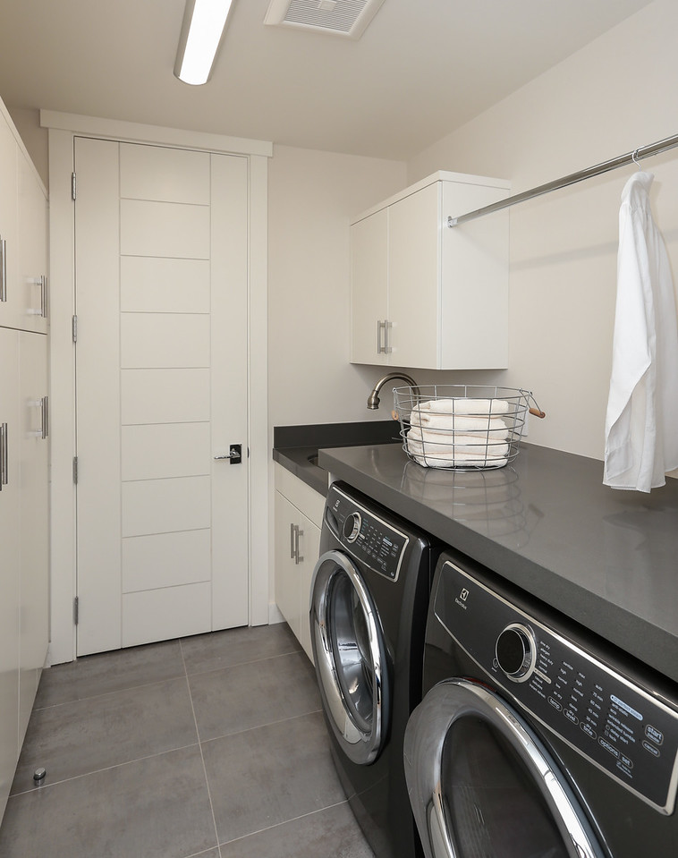 Design ideas for a small contemporary l-shaped dedicated laundry room in San Francisco with an undermount sink, flat-panel cabinets, quartz benchtops, grey walls, porcelain floors, a side-by-side washer and dryer and grey floor.
