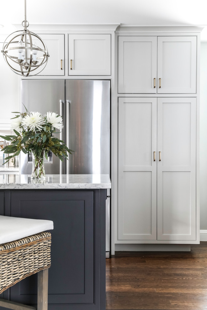 Inspiration for a transitional l-shaped medium tone wood floor and brown floor eat-in kitchen remodel in Boston with a farmhouse sink, beaded inset cabinets, white cabinets, quartz countertops, white backsplash, subway tile backsplash, stainless steel appliances, an island and gray countertops