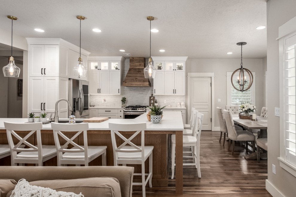Design ideas for a mid-sized country l-shaped eat-in kitchen in Salt Lake City with a drop-in sink, shaker cabinets, white cabinets, quartz benchtops, white splashback, stone tile splashback, stainless steel appliances, medium hardwood floors, with island and white benchtop.