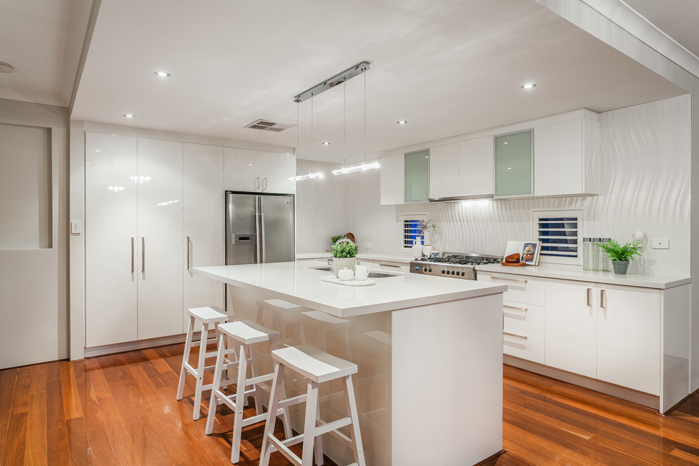 Inspiration for a contemporary l-shaped kitchen in Perth with an undermount sink, flat-panel cabinets, white cabinets, white splashback, stainless steel appliances, medium hardwood floors, with island and white benchtop.